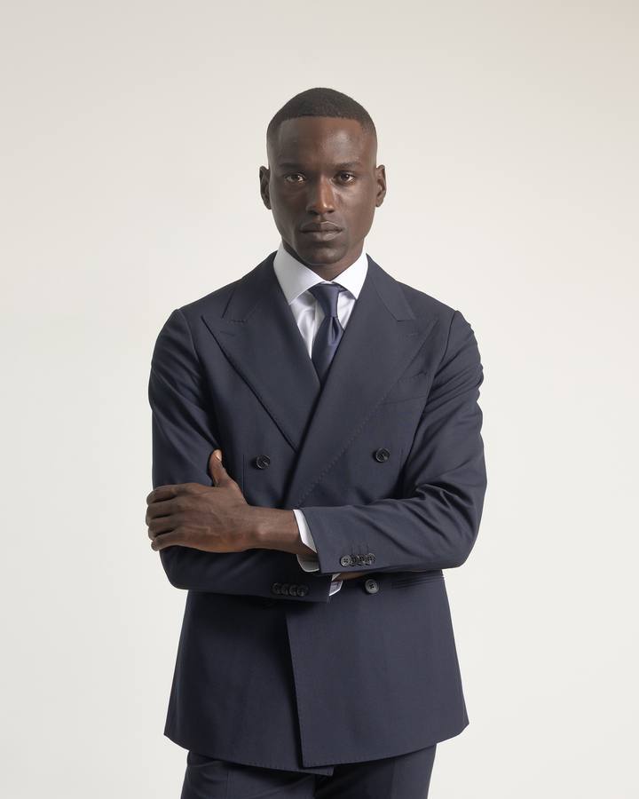 Traje cruzado 6x2 azul marino de PuroEgo en plano medio, con camisa blanca y corbata, de brazos cruzados.