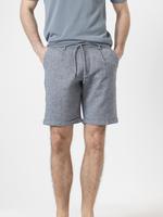 Short de lino azul de PuroEgo, con cordón en la cintura y las manos del modelo en los bolsillos.