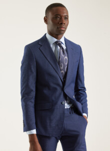 Traje 2 piezas azul marino de micro cuadro, plano medio de tres cuartos con la chaqueta abotonada, camisa celeste y corbata estampada.