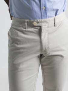 Detalle frontal de pantalón chino marfil con vista de cintura, botón beige y costuras limpias, combinado con camisa a rayas