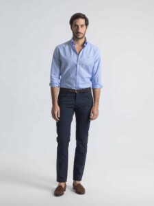 Pantalón azul de cinco bolsillos PuroEgo de frente sobre el modelo, cuerpo entero, con camisa celeste a rayas y mocasines café.