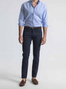 Pantalón azul de cinco bolsillos PuroEgo de frente, de los hombros a los pies, con cinturón de gamuza café y camisa celeste a rayas.