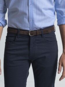 Primer plano de la cintura del pantalón azul de cinco bolsillos: presillas, bolsillos delanteros curvos y cinturón de gamuza café con hebilla plateada.