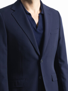 Detalle de la chaqueta azul marino del traje 2 piezas: solapa de muesca, botonadura recta de dos botones y bolsillo de pecho, sobre polo azul.