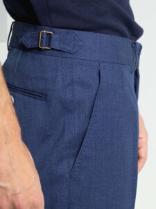 Detalle de la cintura del pantalón azul del traje 2 piezas: hebilla lateral ajustable dorada, pinza y bolsillo trasero con vivo.