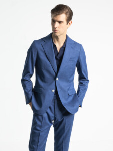 Traje 2 piezas azul de hombre visto de frente, con la chaqueta abotonada y las manos en los bolsillos, sobre un polo azul marino.