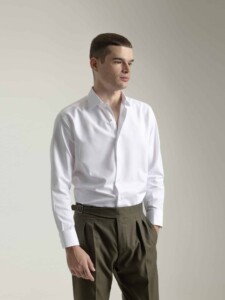 Camisa de vestir blanca PuroEgo en modelo, vista de tres cuartos de frente, con el cuello abierto y pantalón verde oliva con cinturón café.