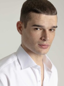 Primer plano del cuello abierto de la camisa de vestir blanca PuroEgo, con el modelo de perfil y el hombro en cuadro, sobre fondo gris claro.