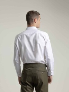 Camisa de vestir blanca PuroEgo vista de espalda en modelo: canesú, manga larga y puño abotonado, con pantalón verde oliva.