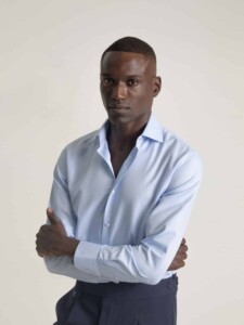 Camisa celeste de vestir PuroEgo, de frente sobre modelo con brazos cruzados y cuello italiano abierto sin corbata, con pantalón azul marino.