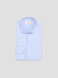 Camisa celeste PuroEgo doblada sin modelo sobre fondo gris, con la etiqueta PUROEGO en el cuello italiano y el puño apoyado al frente.