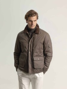 Chaqueta field kaki PuroEgo con cuello de pana café levantado, vista de frente en modelo con las manos en los bolsillos y pantalón blanco.