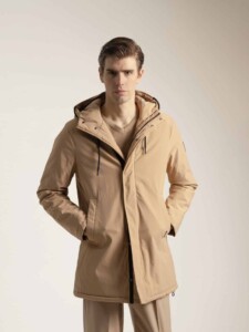 Abrigo beige con capucha PuroEgo visto de frente sobre el modelo, abierto, con cierre negro a la vista y las manos en los bolsillos.