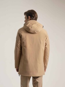 Abrigo beige con capucha PuroEgo visto de espalda: espalda lisa, capucha bajada, parche negro en la manga y cordón en el ruedo.