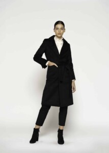 Vista frontal completa de abrigo negro largo con solapas amplias, cinturón a la cintura, combinado con blusa blanca y pantalón negro
