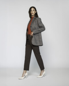 Vista lateral de blazer a cuadros grises con dos botones, combinado con pantalón marrón y suéter teja, modelo Formentera