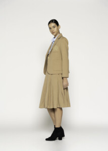Vista lateral de blazer camel con bordado en el pecho, solapa clásica y bolsillos frontales, combinado con falda plisada