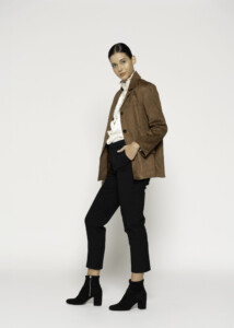 Vista lateral de blazer camel efecto ante con textura suave, manos en bolsillos, combinado con camisa blanca y pantalón negro