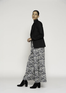Vista lateral de blazer negro con cuello alto cerrado y corte oversize, combinado con falda estampada y botines