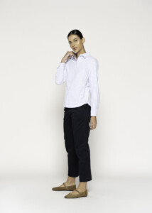 Vista lateral de tres cuartos de blusa a rayas finas azules y blancas con cuello clásico, combinada con pantalón negro y flats beige