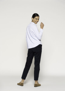 Vista de tres cuartos desde atrás mostrando la caída de la blusa a rayas finas con cuello clásico y pantalón negro, modelo Formentera