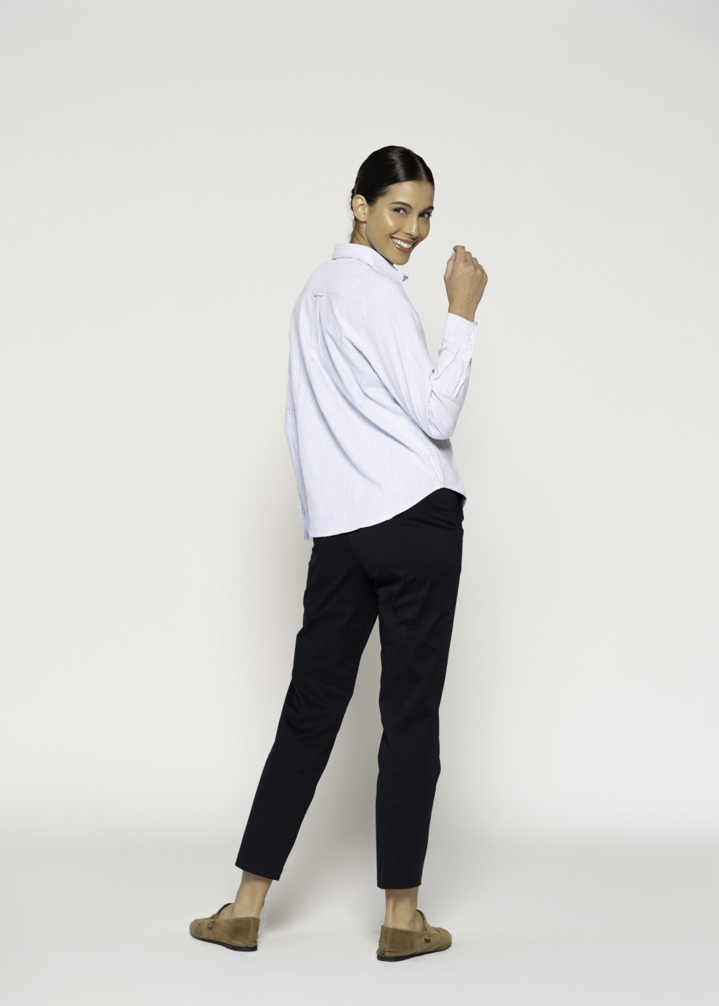 Vista de tres cuartos desde atrás mostrando la caída de la blusa a rayas finas con cuello clásico y pantalón negro, modelo Formentera