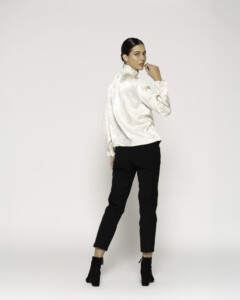 Vista trasera tres cuartos de blusa beige satinada con cuello alto y mangas con volados, combinada con pantalón negro