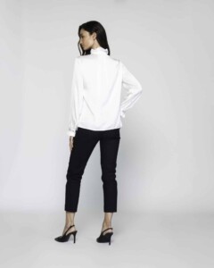 Vista posterior de blusa blanca con cuello volante y puños abotonados, combinada con pantalón negro y tacones