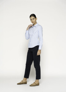 Vista lateral de blusa celeste con cuello camisero y botonadura frontal, combinada con pantalón negro y flats beige