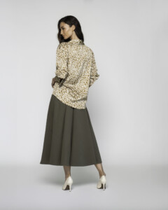 Vista de espalda de blusa estampada con motivos orgánicos beige y dorado, combinada con falda midi verde oliva y tacones claros