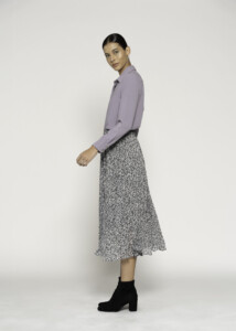 Vista lateral de blusa lila de manga larga con cuello clásico, combinada con falda plisada estampada y botines negros