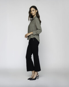 Vista lateral de blusa verde oliva con cuello camisero, manga larga y corte amplio, combinada con pantalón negro y stilettos