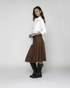 Vista lateral de camisa blanca oversize con manga 3/4, cuello clásico y largo asimétrico, combinada con falda marrón
