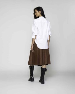 Vista trasera de camisa blanca oversize con mangas 3/4 anudadas y bajo asimétrico, combinada con falda plisada marrón modelo Formentera