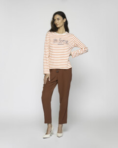 Vista completa de camiseta a rayas naranjas y blancas con bordado "St. Tropez", combinada con pantalón marrón y stilettos