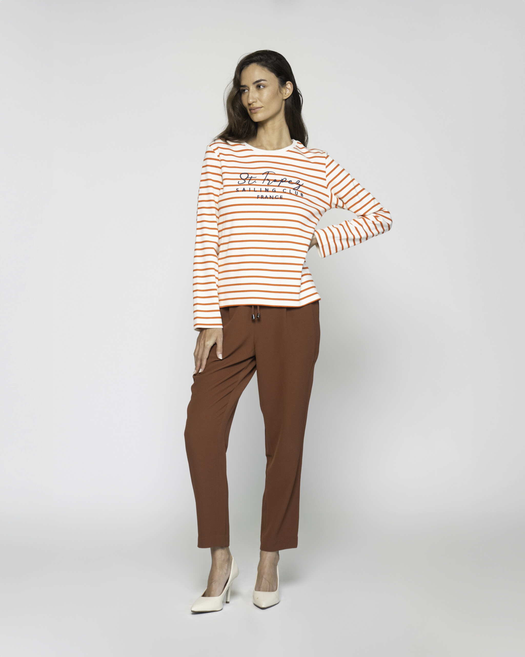 Vista completa de camiseta a rayas naranjas y blancas con bordado "St. Tropez", combinada con pantalón marrón y stilettos