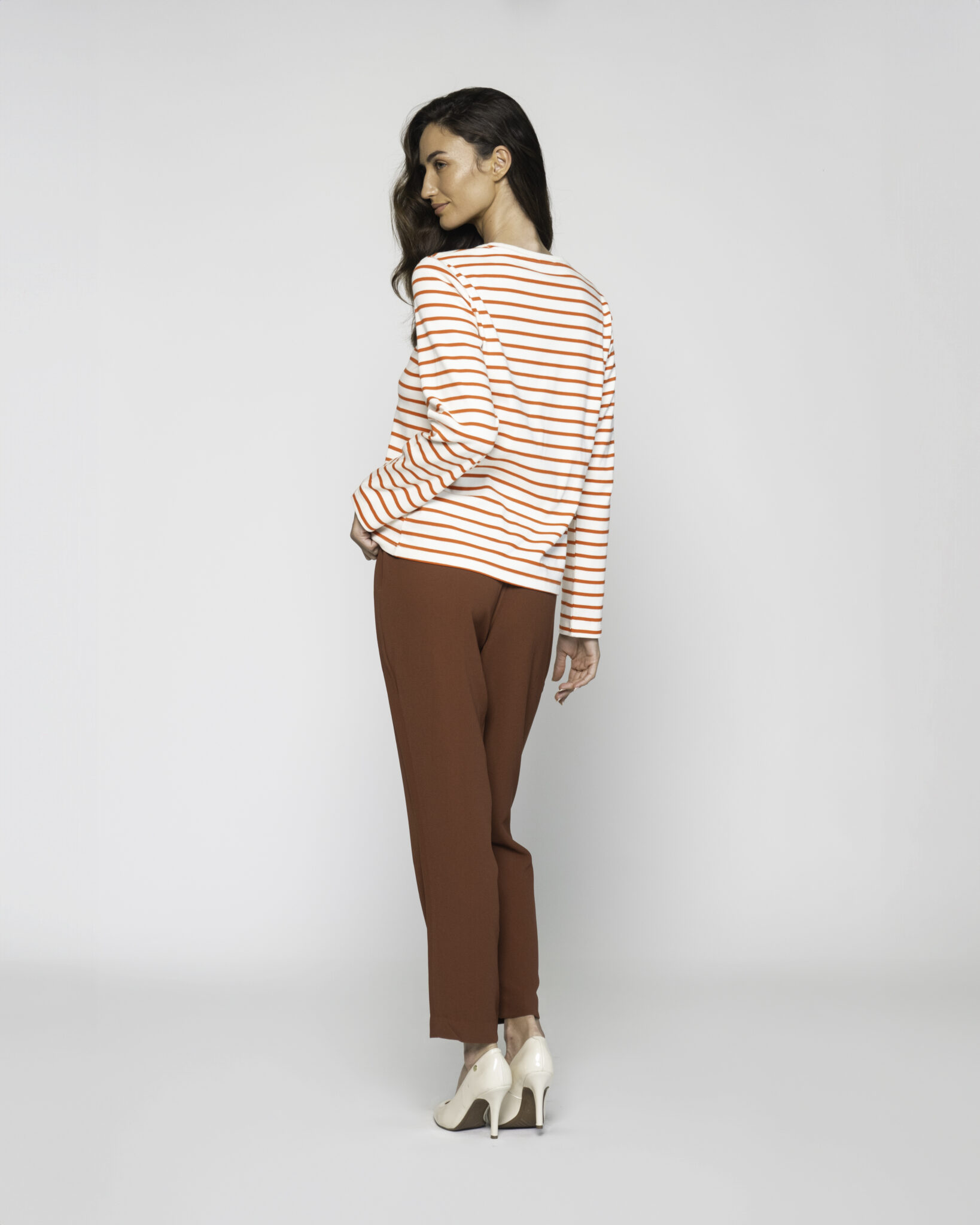 Vista de espalda de camiseta a rayas horizontales blancas y naranjas con manga larga, combinada con pantalón marrón
