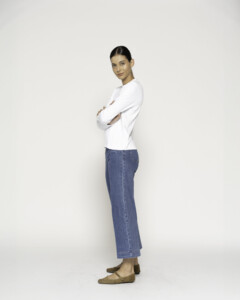 Vista lateral de camiseta blanca manga larga con jeans azules de pierna ancha, brazos cruzados, modelo Formentera