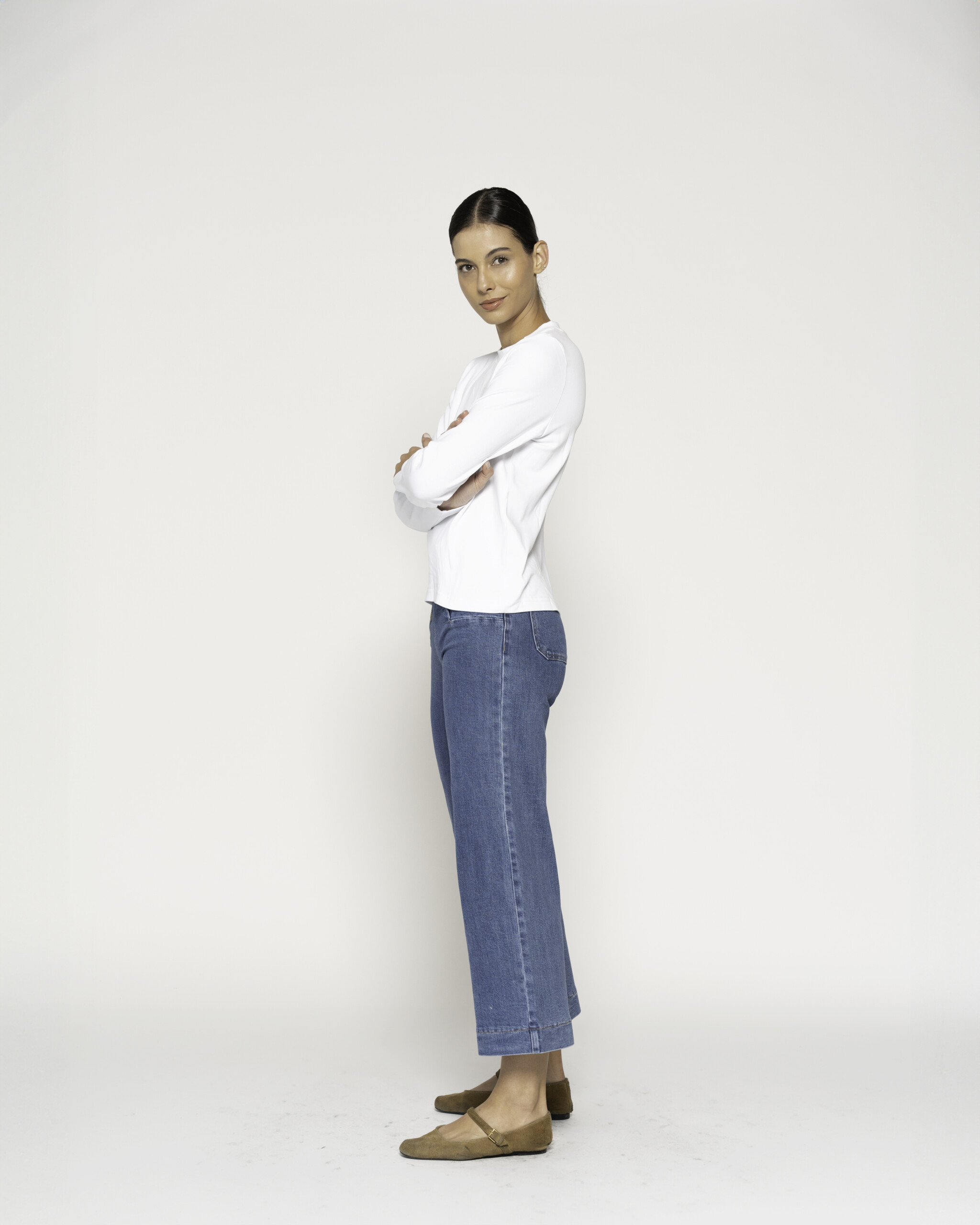 Vista lateral de camiseta blanca manga larga con jeans azules de pierna ancha, brazos cruzados, modelo Formentera