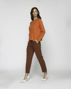 Vista lateral de camiseta naranja manga larga con cuello redondo, combinada con pantalón marrón y stilettos blancos