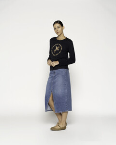 Vista completa de cuerpo entero mostrando camiseta negra con estampado de pegaso dorado combinada con falda denim midi con abertura frontal, modelo Formentera