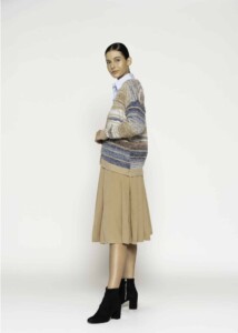 Vista de perfil del cárdigan a rayas beige y azul combinado con camisa blanca y falda plisada camel, modelo Formentera