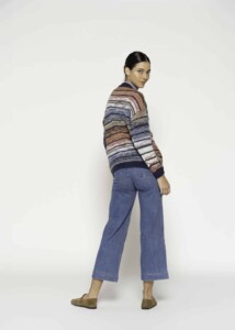 Vista de tres cuartos trasera de cardigan a rayas horizontales multicolor en tonos azul, beige y naranja, combinado con jeans culotte