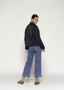 Vista de espalda de chaqueta acolchada azul marino con costuras diagonales y puños en contraste, combinada con jeans