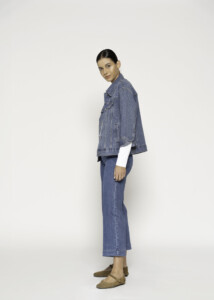 Vista lateral de chaqueta denim azul con tachas plateadas dispersas, combinada con jeans y top blanco, modelo Formentera