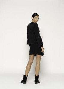 Vista de espalda de chaqueta negra de corte recto, con cuello redondo y manga larga, modelo Formentera con botines