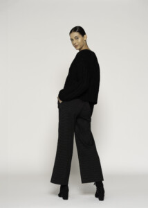 Vista de tres cuartos trasera mostrando sweater negro de punto grueso texturizado y pantalón con rayas diplomáticas, modelo Formentera