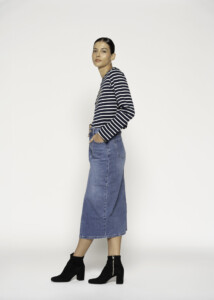 Vista lateral de falda denim midi azul medio con abertura frontal visible, combinada con suéter a rayas y botines negros