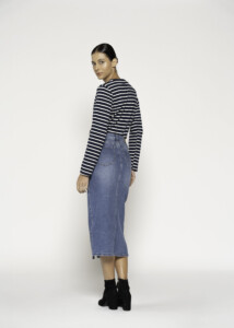 Vista de espalda de falda midi denim azul con bolsillos traseros visibles, combinada con remera a rayas marineras, modelo Formentera