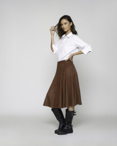 Vista lateral de falda midi marrón con vuelo amplio y textura suave, combinada con camisa blanca y botas altas negras